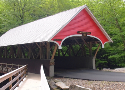 [Covered bridge with a red end-cap used for buses transporting visitors to the Flume. To the left and outside of it is an uncovered wooden walkway for pedestrians.]